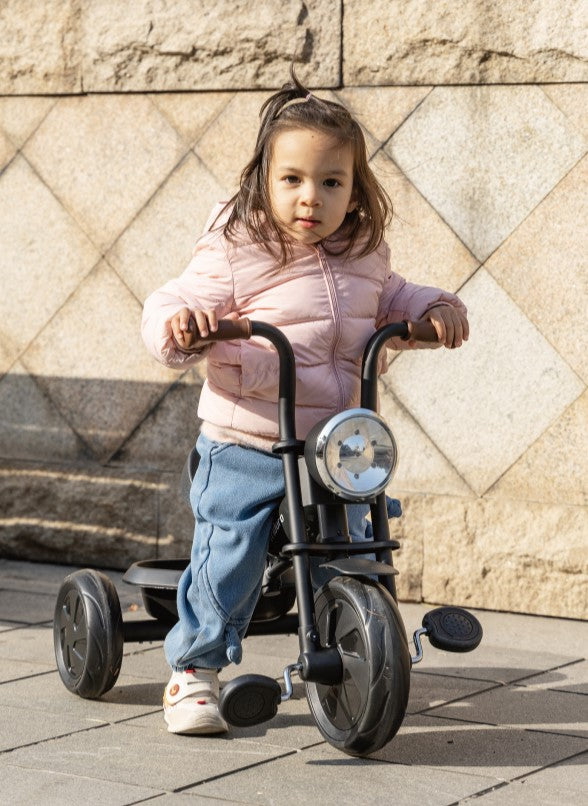 Child riding a tricycle against a stone wall.